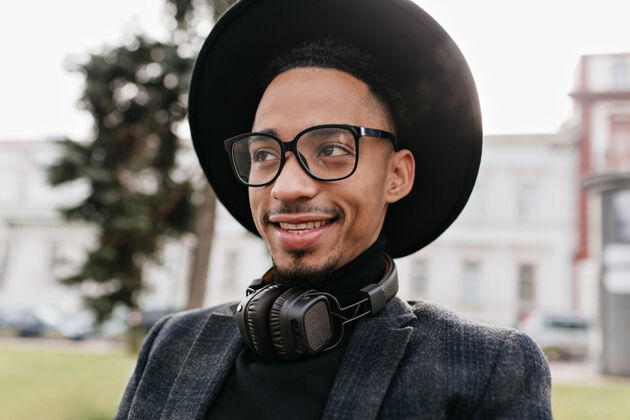 配饰迷人的非洲男人带着真诚的微笑摆姿势戴着眼镜和耳机的可爱黑人男模的户外照片非洲白天肖像