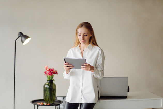 肖像一位年轻的金发女商人在办公室里拿着笔记本电脑和手机在室内工作欢呼女性公司