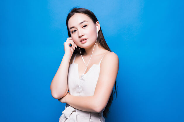 女士美丽的肖像年轻的亚洲妇女听电话音乐与耳机隔离在蓝色的墙壁上耳机肖像快乐