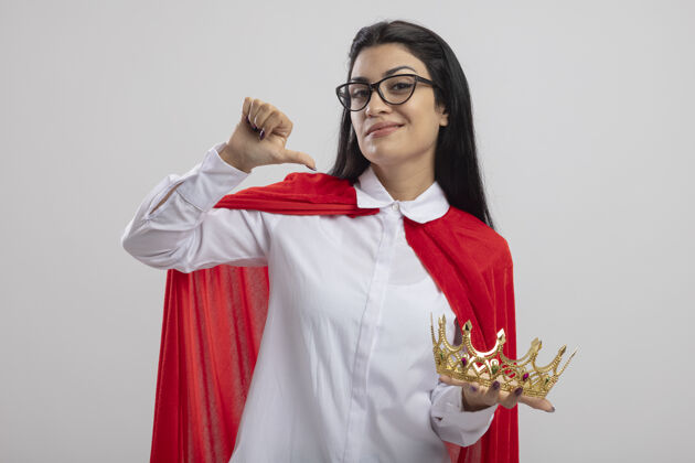 年轻自信的年轻女超人戴着眼镜举着皇冠看着前面指着自己孤零零的白墙上感觉超级英雄衣服
