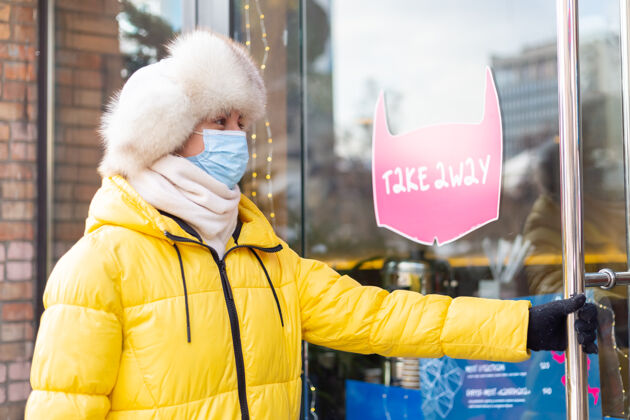 外卖食品在寒冷的冬日 快乐的年轻女子在餐厅门口 刻字 吃外卖窗户流行病防护口罩