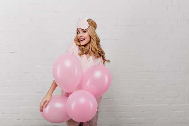 肖像戴着睡衣的快乐女孩站在白色的墙上 手里拿着派对气球一幅美丽的年轻女士在周末早晨庆祝的画像气球放松漂亮