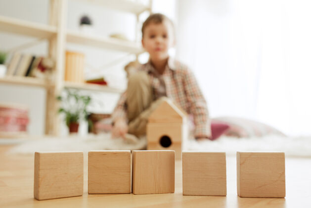 教育小孩子坐在地板上漂亮的男孩在家里玩木块堆栈活动房间