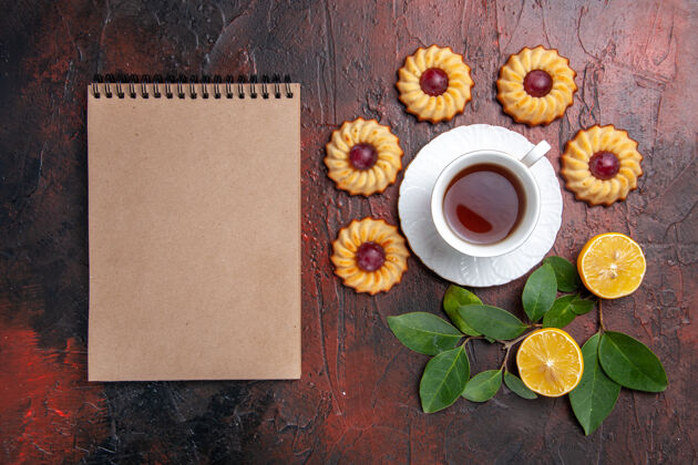 笔记本顶视图一杯茶加上小饼干放在深色的桌子上甜点饼干甜顶部茶杯雏菊
