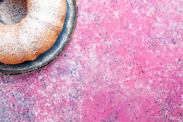 可口糖粉蛋糕圆的俯视图形成在粉红色的光表面质地面团生的