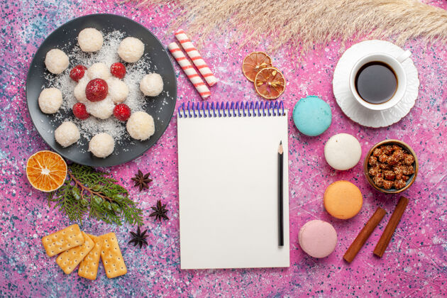 脸粉美味的椰子糖和麦卡龙的俯视图和浅粉色表面上的一杯茶椰子糖Rouge