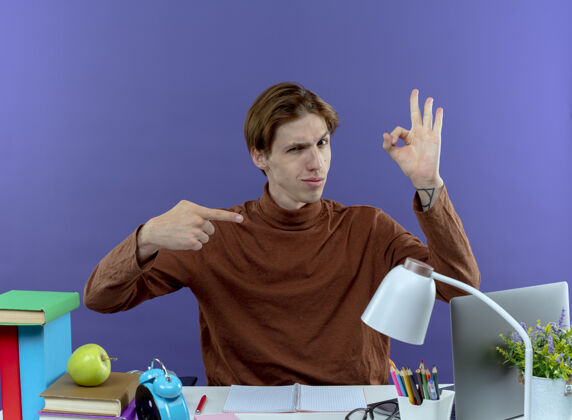 好的坐在书桌旁 手里拿着各种各样的学习工具 摆出一副很好的姿势 指着紫色的手指书桌坐着点