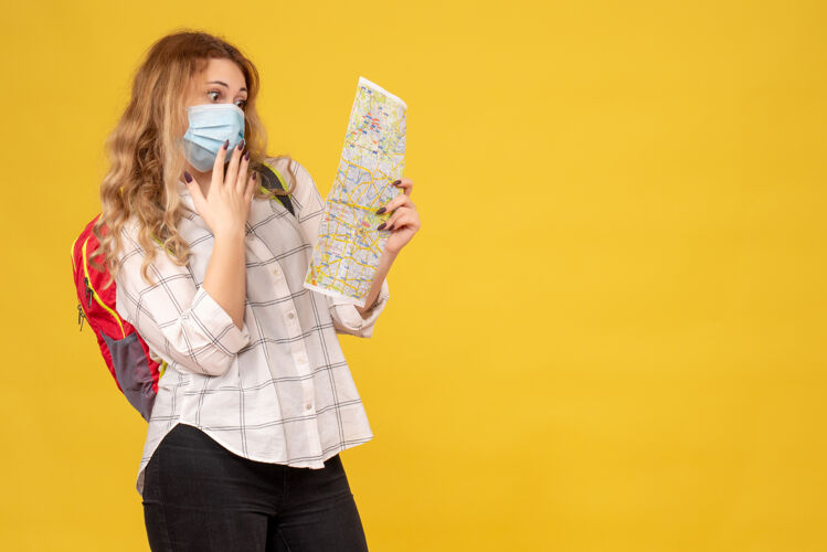 背包顶视图惊讶的旅行女孩戴着她的面具和背包在看黄色的地图脸人成人
