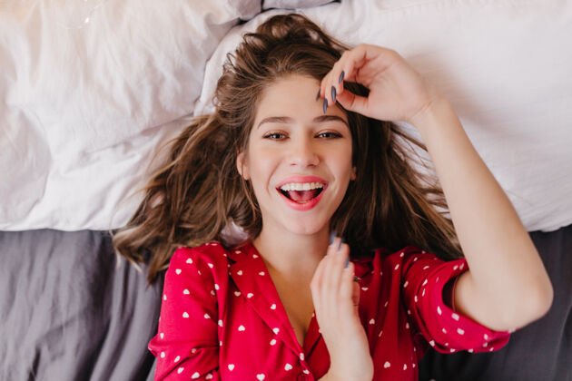 睡觉时间身着红色睡衣的快乐年轻女子的头顶照片懒散微笑的欧洲女孩的室内肖像微笑放松成人