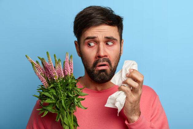 个人胡须男患有过敏性鼻炎 拿着餐巾不高兴地看着过敏原 感觉不舒服 流鼻涕 不断打喷嚏 需要有效的药物治疗疾病感觉年轻组织
