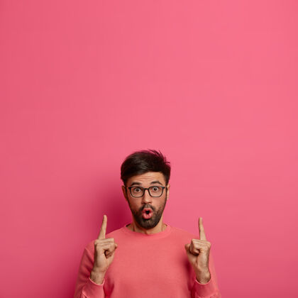 跳投惊骇震惊的男顾客被机会公告迷住了 用惊奇的表情指着上面 展示广告的空白 展示惊人的销售 孤立在粉红色的墙上拼图折扣不知道