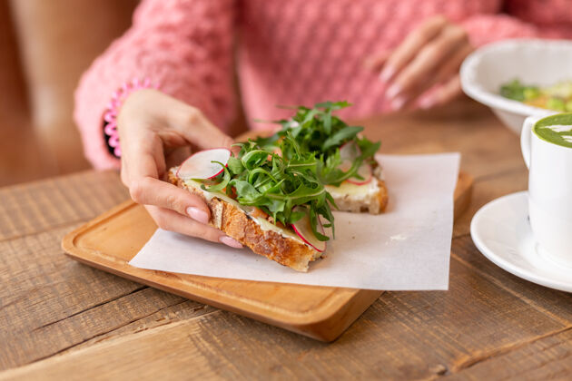 小吃一位女士穿着一件温暖舒适的毛衣在一家餐厅享用健康的早餐 烤面包配芝麻菜和三文鱼食物午餐沙拉