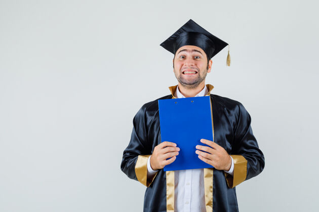 休闲年轻人拿着毕业制服的剪贴板 看上去很高兴前视图毕业胡须前面
