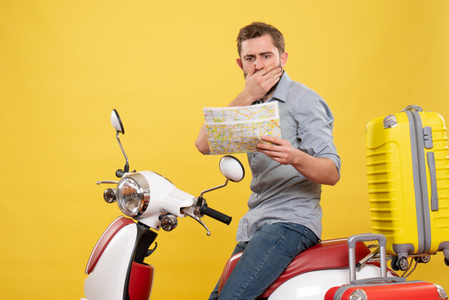 微笑旅游概念与困惑的年轻人坐在摩托车上 手提箱上 拿着黄色地图持有输送机旅行