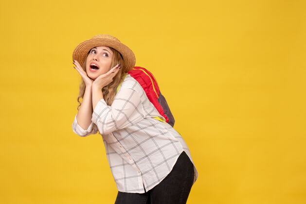 红色顶视图微笑的旅行女孩戴着她的帽子和红色背包在黄色的相机摆姿势微笑漂亮成人