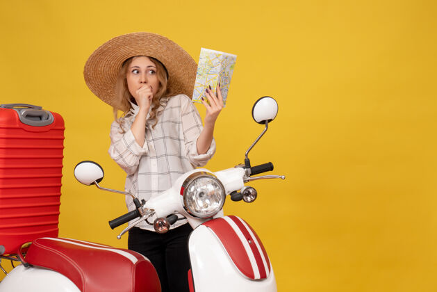 摩托车俯视图：一个戴着帽子的年轻女子坐在摩托车上拿着地图 正在收行李行李抱着摩托车