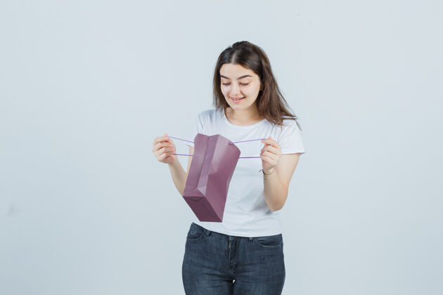 女人年轻女孩看着一个纸袋在t恤 牛仔裤和看起来很高兴前视图人漂亮成人
