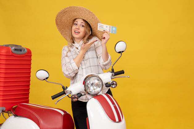 微笑前视图微笑的年轻女子戴着帽子收集她的行李坐在摩托车上 并显示票行李传送带收集