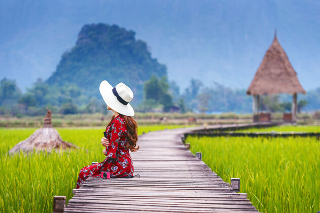 全景老挝万荣 坐在绿油油的稻田木路上的年轻女子村庄水稻冒险