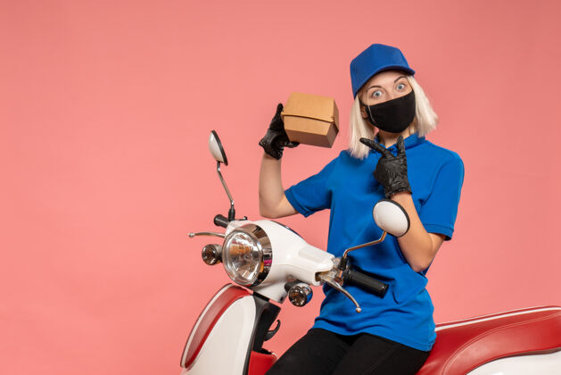 服务正面图：戴着面具的女快递员 粉红色的小食品包装人员女信使食品