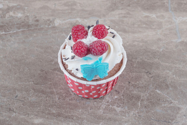 顶部一个奶油和浆果盖在大理石上的纸杯蛋糕口感纸杯蛋糕浆果