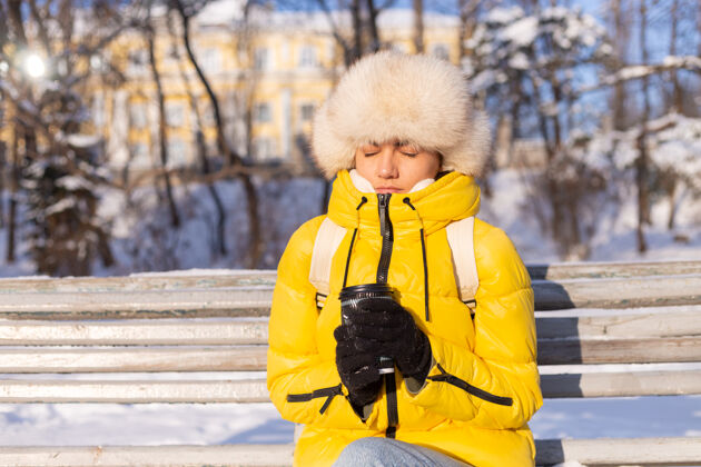 时尚一个冬天的女人 穿着暖和的衣服 在一个阳光明媚的日子里 坐在长凳上 冻得浑身发冷 冬天很不开心 一个人拿着咖啡悲伤愤怒肖像