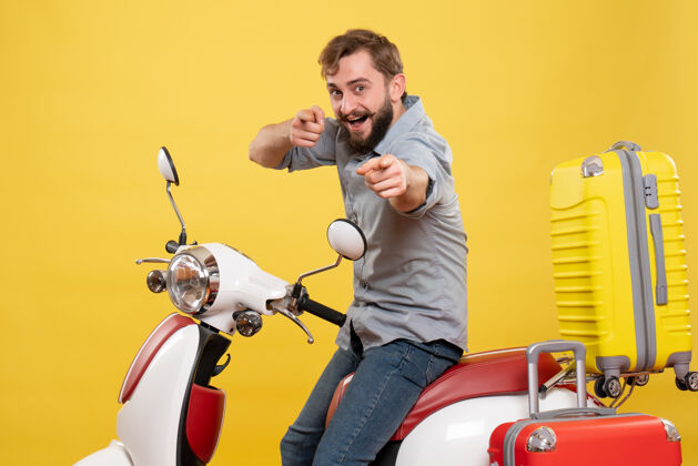 车辆旅游概念与年轻的微笑胡须男子坐在摩托车上 并指出它的黄色前进旅行指向自行车