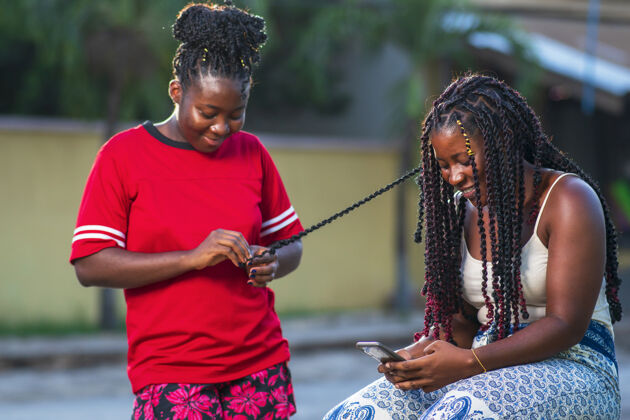 手机两位非洲裔美国女性朋友微笑着在户外编辫子朋友漂亮辫子