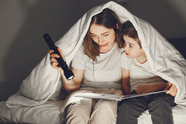 家庭母子俩在毯子下躺在床上看书一起玩耍夜晚