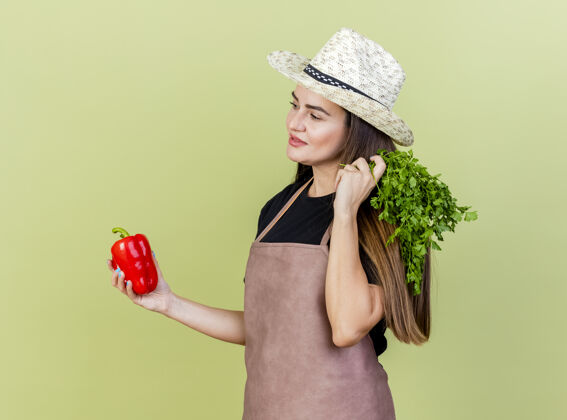 橄榄看着一旁高兴的漂亮园丁 身着制服的女孩戴着园艺帽 手里拿着辣椒和香菜 背景是橄榄绿花园举行壁板