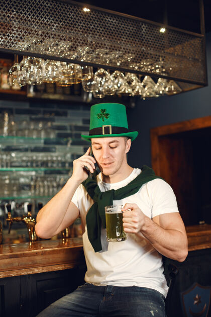 节日酒吧里的男人拿着啤酒男人庆祝圣帕特里克节戴着绿色帽子的男人啤酒啤酒马克杯