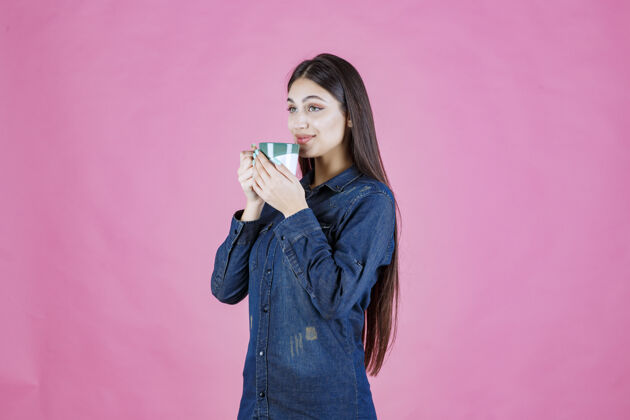 冬天年轻女子拿着一个白绿色的咖啡杯 闻着品味成人温暖