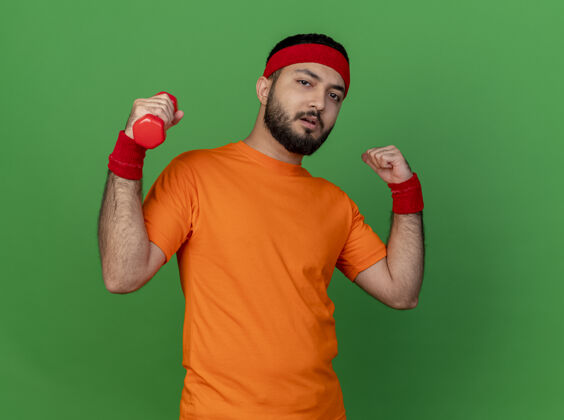 运动自信的年轻运动型男子戴着头带和腕带练习哑铃显示出强烈的姿态隔离在绿色背景上锻炼自信年轻