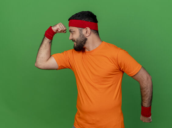 腕带自信的年轻人戴着头带和腕带 在绿色背景上显示出强烈的姿态姿态自信强壮