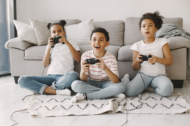 小玩电子游戏的非洲孩子穿着轻便衣服的孩子孩子手里拿着控制器沙发家庭房间