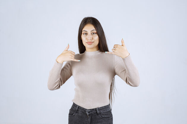 雇员穿灰色毛衣的女孩在做竖起大拇指的招牌享受年轻人服装