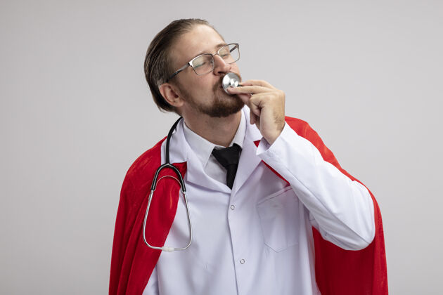 吻年轻的超级英雄穿着医用长袍 戴着听诊器和眼镜 在白色背景上亲吻听诊器小伙子超级英雄医生