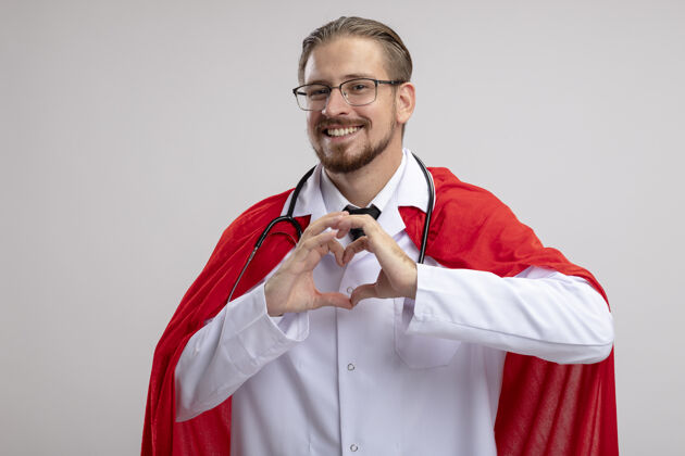 手势微笑着的年轻超级英雄 穿着医用长袍 戴着听诊器和眼镜 在白色背景上显示出孤立的心脏姿势心脏年轻人男人