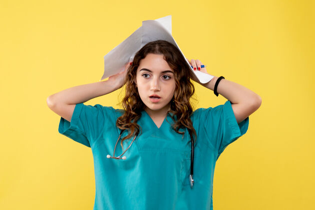 女性正面图女医生穿着医用衬衫拿着纸黄色办公桌大流行病毒制服covid-19情绪分析漂亮成人纸