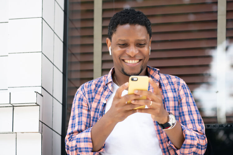 城市坐在街上商店橱窗边用手机的非裔美国人城市概念肖像男性快乐
