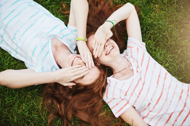 在一起一对孪生姐妹闭上眼睛躲避阳光 在夏日躺在地上年轻欢呼朋友