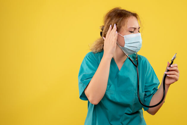 女医生黄色墙上穿着医疗服 戴着听诊器面罩的女医生的正视图人电话面罩