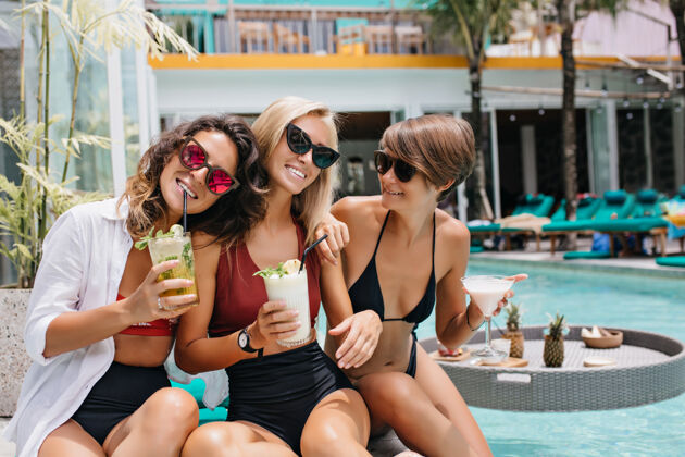 泳装浪漫的黑发女人 戴着粉红色的眼镜 在和朋友拍照时喝着鸡尾酒迷人的女士在泳池里度过周末热配件比基尼