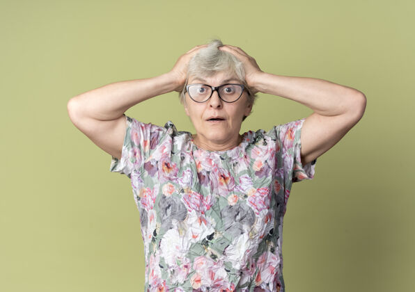 眼镜震惊的戴眼镜的老妇人把头孤立地放在橄榄绿的墙上老年人眼镜手持