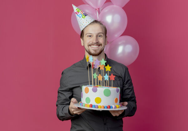抱着戴着生日帽的笑脸帅哥手持氦气球站在那里拿着生日蛋糕氦微笑站着