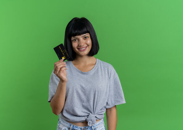 持有笑容可掬的年轻黑发高加索女孩拿着信用卡绿色复制空间