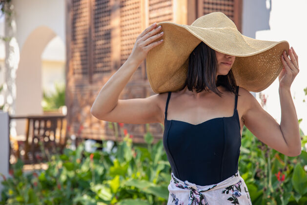 休息在一个炎热的夏天 一个戴着大草帽的女孩站在一栋旧房子的正面附近时尚女人乡村