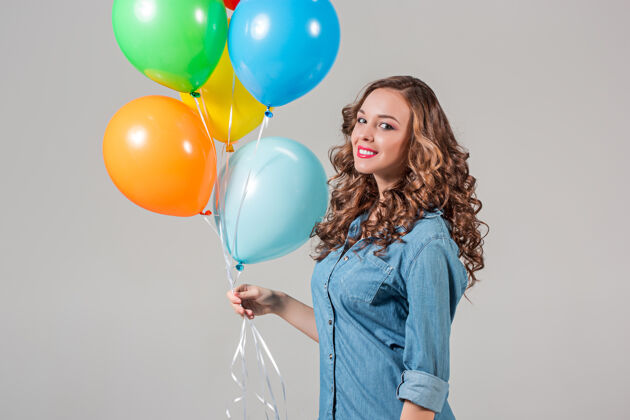 欢乐在灰色的工作室墙上拿着彩色气球的年轻女子华丽脸年轻