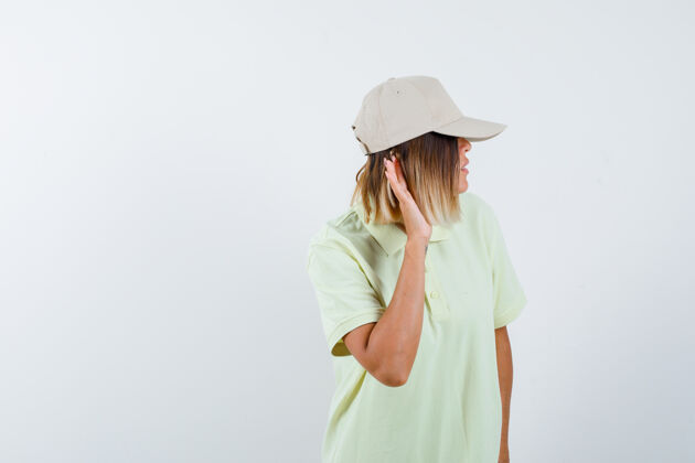 面部年轻女孩手拉手靠近耳朵 穿着t恤和帽子 专注地看着前方帽子身体年轻