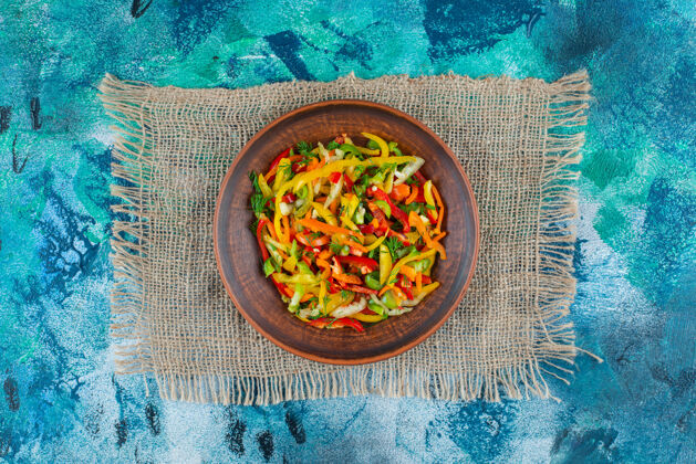 新鲜蔬菜沙拉放在盘子里的粗麻布上 蓝色背景欧芹蔬菜美味